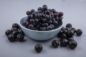 top view of fresh and sweet flavour black grapes on a blue bowl on a grey background