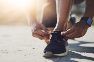 Hands, black man and sneakers with laces outdoor for fitness support, reading and running exercise of marathon. African, male athlete and sports shoes for workout, training and morning adventure